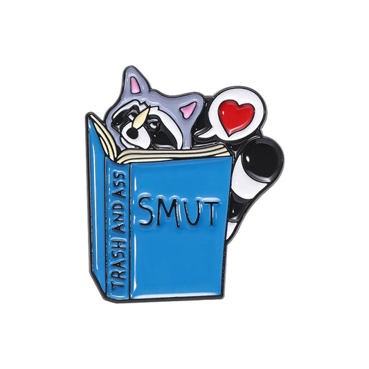 Racoon reading a smut book enamel pin
